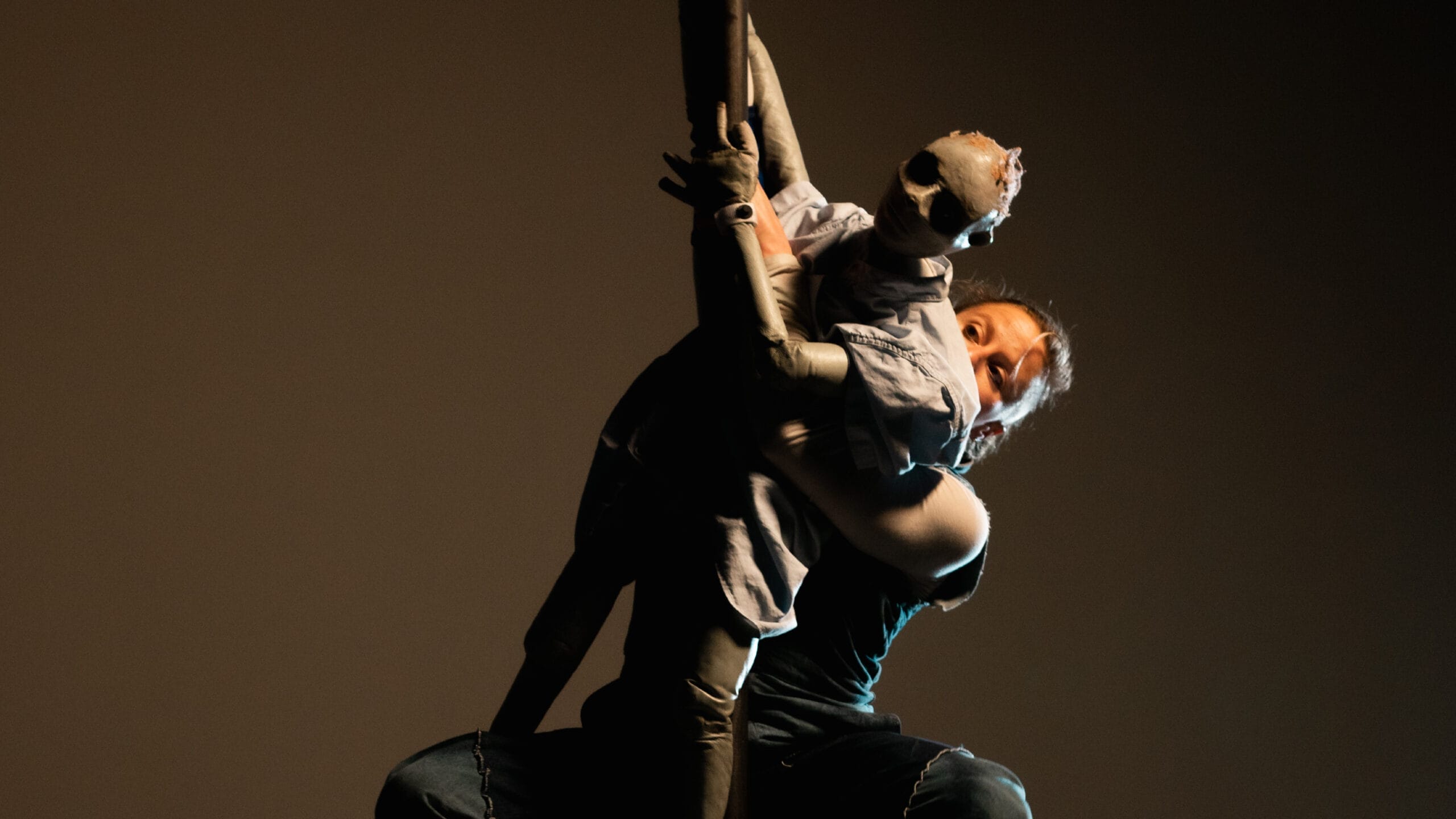 A person performs with a human-like puppet, both suspended against a dark background.