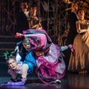 A theatrical dance scene with a man dramatically dipping a woman in a colourful dress and striped stockings.