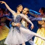 A male and female ballet dancer in ornate blue costumes perform a duet on stage