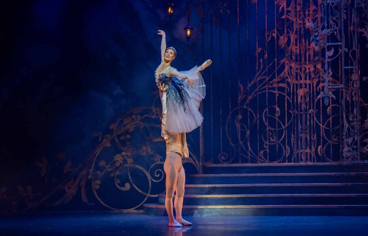 A ballerina in a blue dress is lifted high by a male dancer on stage.