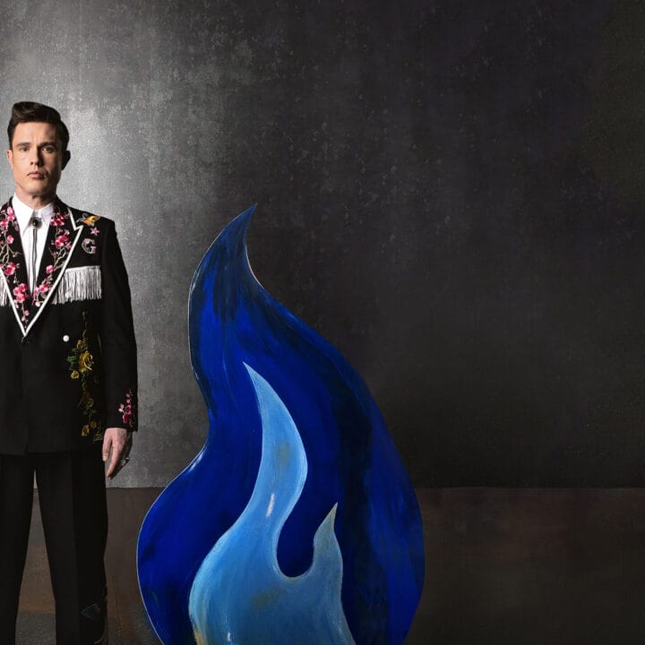 Ed Gamble wearing a fancy suit with custom embroidery, behind some blue flames