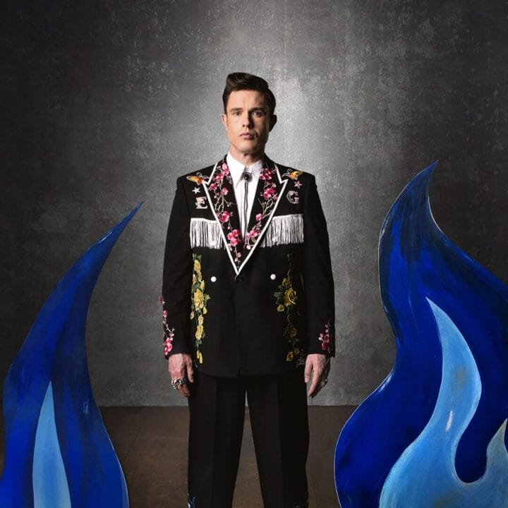 Ed Gamble wearing a fancy suit with custom embroidery, behind some blue flames