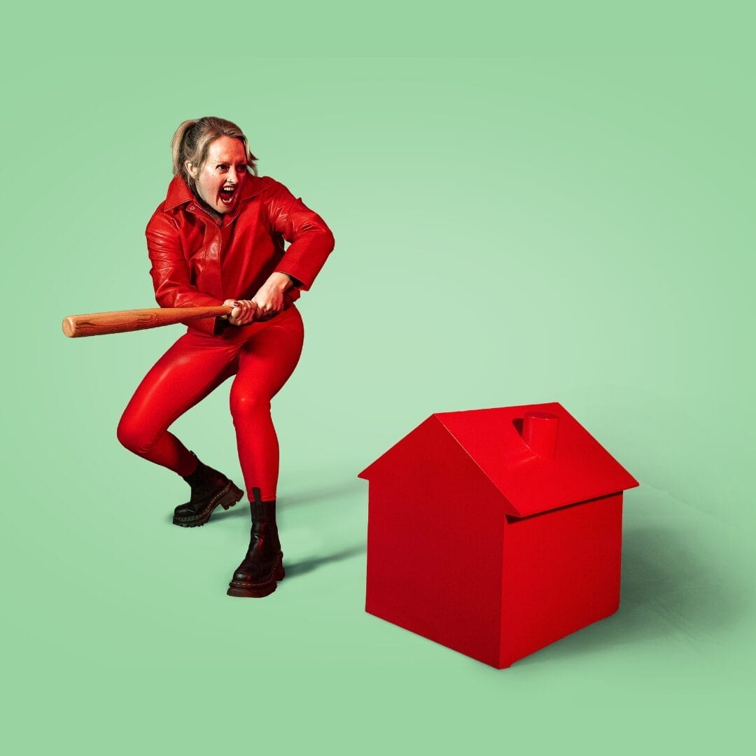 A person in a red outfit holds a wooden bat, appearing ready to hit a red house-shaped object.
