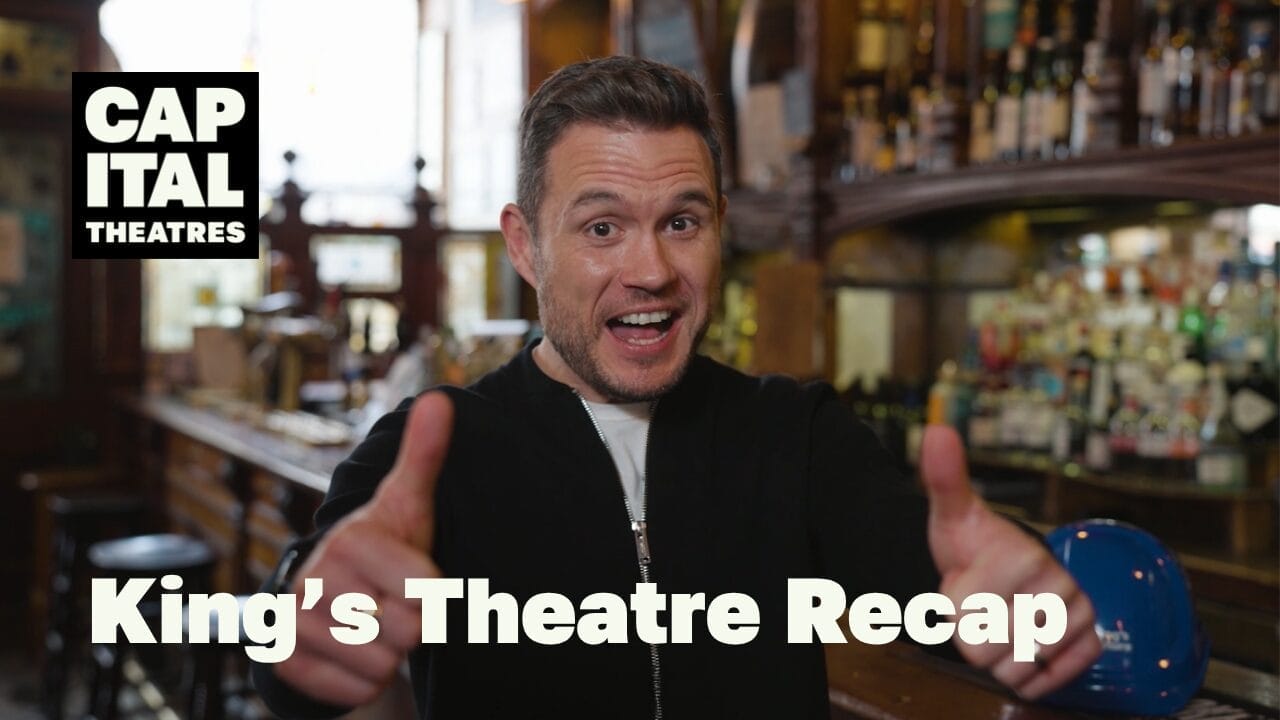A man in a black jacket stands in a bar, giving two thumbs up and smiling. The text "CAPITAL THEATRES" and "King's Theatre Recap" appears over the image, with shelves of bottles and glassware—each one holding hope in a bottle—in the background.